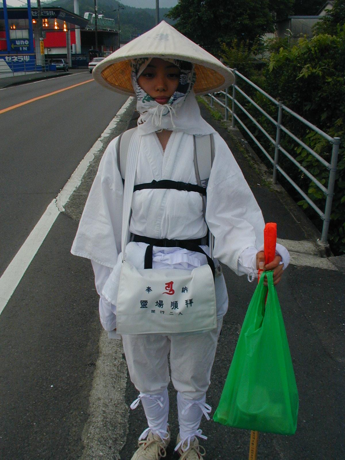 白衣・菅笠・金剛杖のお遍路さん。袋には「同行二人」